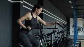 Young active woman spinning air bike in gym. Brunette female training on air bike in slow motion. Medium shot of fitness girl working out with copy space - Powered by Shutterstock - Get 15% off with code: PIKWIZARD15