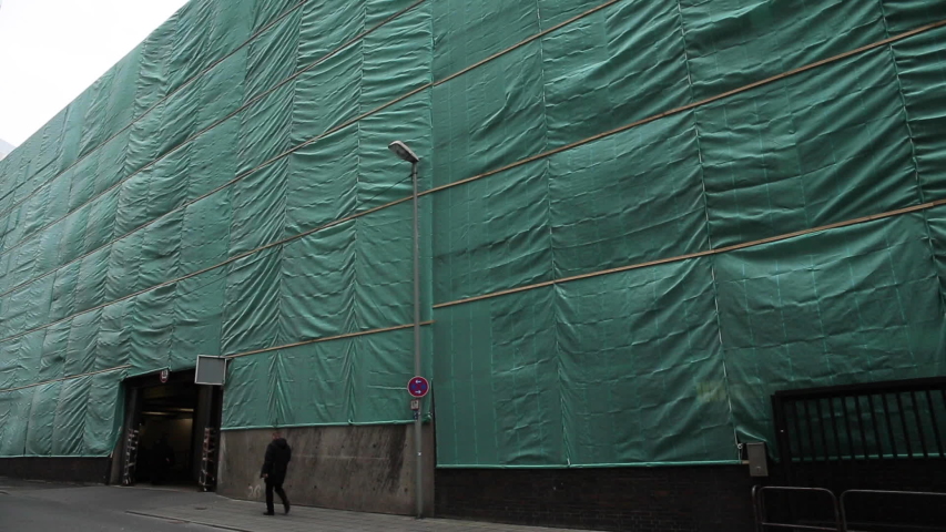 Green scaffold netting covering building on sidewalk. Long shot.