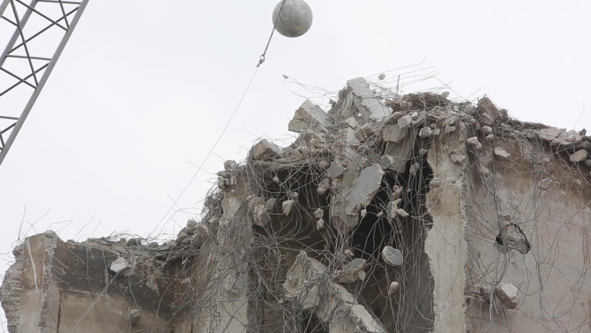 Wrecking ball slamming down over building debris.