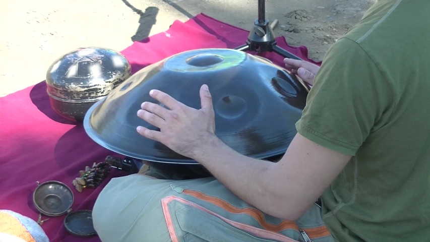 Young man plays a Hang musical instrument. Red rug. View from the side. Smoke, mystical objects, glare of the sun. The concept of Relaxation and tranquility.