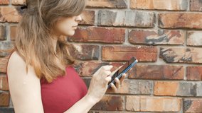 young woman with a phone on the background of a brick red wall, the girl is on the Internet, communicates in the network, technology and lifestyle