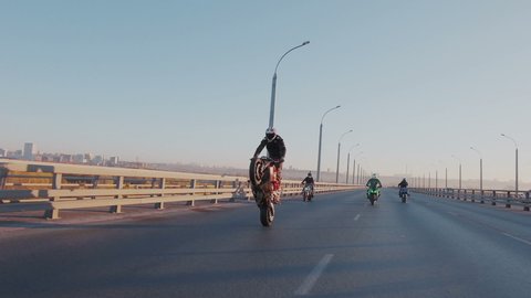 Slow motion. Several daring crazy motorcyclists perform stunts on the empty highway. Stunt rider rides forward on the back wheel. He enjoy and gets adrenaline. Extreme lifestyle.
