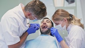 Handsome brunette man smiling while having dental procedure with dentist and assistant at the dental clinic