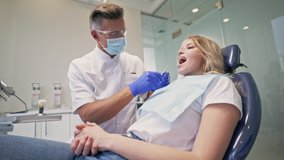 Concentrated blond woman listening dentist about problem with her tooth while looking at the dummy tooth and at the screen after checking-up procedure in the dental clinic