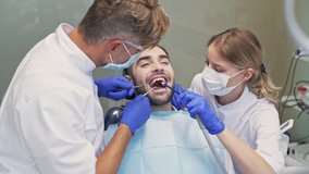 Attractive brunette man sitting in chair while having dental procedure with dentist and assistant at the dental clinic