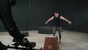 Handheld shot of strong young sportsman performing box jumps when demonstrating physical exercises for sports video