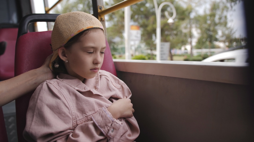 Little girl wrapped in a jacket on the bus with no Windows and looks outside.