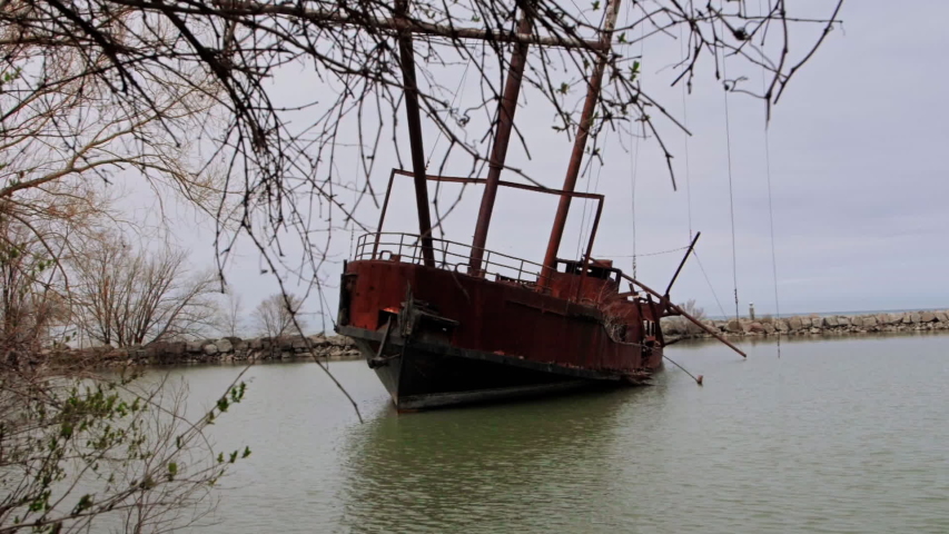 Rusty red shipwreck stuck in shallow green water. Old and abandoned rust covered metal pirate style ship.