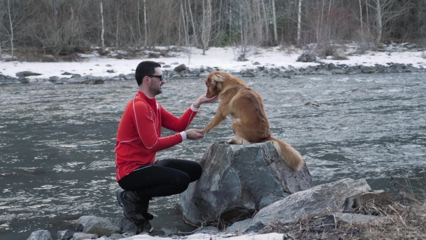 A man in red giving his Scottish Retriever dog with a treat during obedience training in the nature next to a flowing river in France SLOW MOTION.