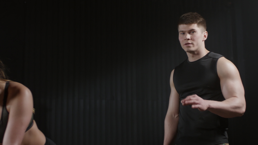 Fit young woman performing incline push ups in dark room and man talking to camera while they recording video blog about sports