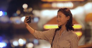 Pretty young asian woman female tourist looking at mobile phone taking picture at night city in Chengdu Jiuyan Qiao Sichuan China with urban neon light in the background