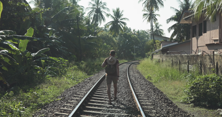 Traveler man with backpack walking between two railway lines
