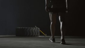 Sequence of shots of strong young man walking through dark room and hitting large tractor tire with sledgehammer when recording video for sports blog