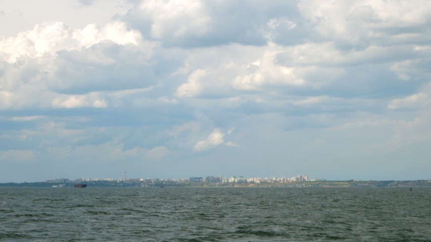 Swell Black Sea with waves, the coastline with buildings of city in the distance and the beautiful sky with dramatic clouds near Odessa in Ukraine. Seascape.