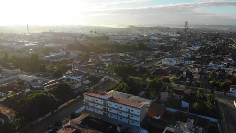 Sunset Aerial shot of a low-income urban area in Cruz das Almas, Bahia, Brazil. Show houses, small buildings in the neighborhood, and green environnement. Drone slowly moving up.
