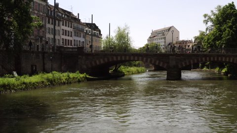 The Pont Kuss in Strasbourg at daytime. People are walking to and from the city center on a sunny day. The drone is rising into the French sky.