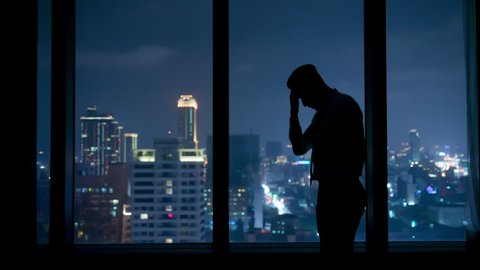silhouette of upset businessman standing by the window at night