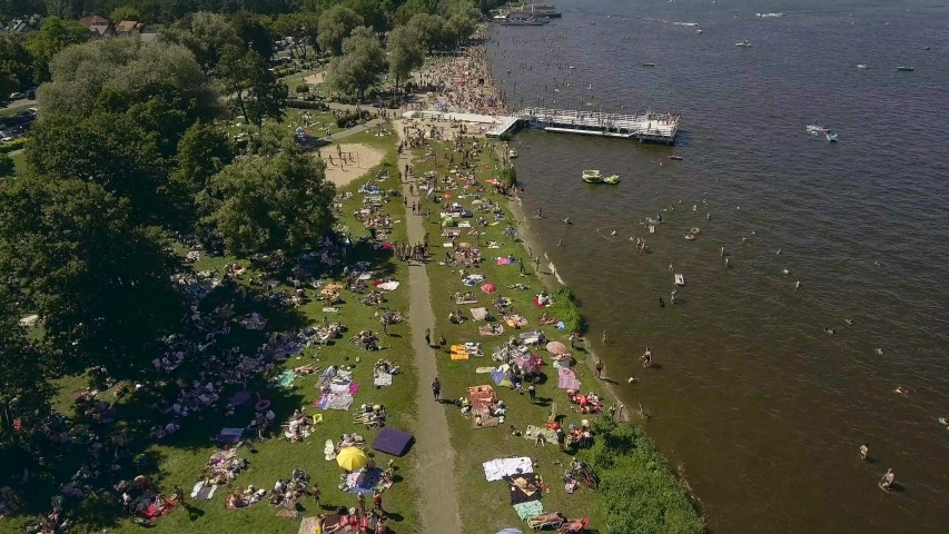 4K. AERIAL VIEW. People sunbathe on the beach on the lake shore in a suburb of Warsaw / Poland. Top view of the crowd of people sunbathing on the beach at the lake.