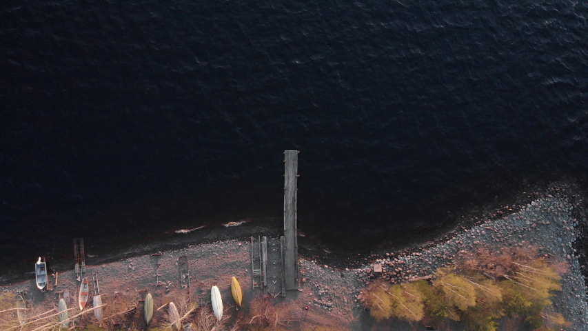 Aerial, top down, drone shot, static, above a man walking, on a wooden pier, at Vuoniemi cape, at lake Saimaa, on a sunny, spring evening, in North Karelia, Finland