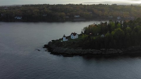 Slow AERIAL slide by the Curtis Island Lighthouse with misty golden sunset light in the background.