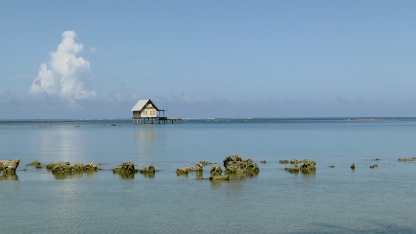 House on stilts in the sea with waves breaking in the background in French Polynesia. Locked off and wide angle