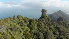 Drone flying towards a tall rock formation on top of a mountain on a remote island