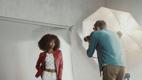 Backstage of the Photo Shoot: Make-up Artist Applies Makeup on Beautiful Black Model, in a Moment Photographer Starts Taking Photos with Professional Camera. Fashion Magazine Studio Photoshoot