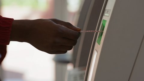 Close-up of african american black man's hand removing a credit card from a cash dispenser. Young man using an ATM machine inside the bank.