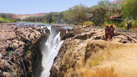 NAMIBIA - CIRCA 2018 - Aerial reveals two Himba tribal women girls in front of Epupa waterfalls on the Angola Namibia border, Africa.