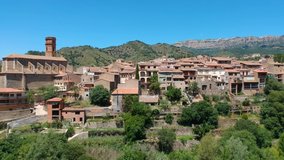Medieval town with a tower on the background of high mountains on a sunny day, aerial video.