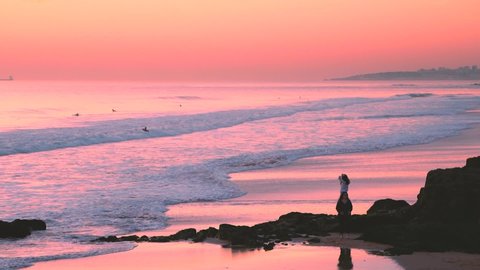 Carcavelos, Portugal - 12/31/18: Incredibly beautiful pink sunset sky reflections, atlantic ocean waves at Carcavelos beach, Orange pink tones, Man walking in low tide water waves.