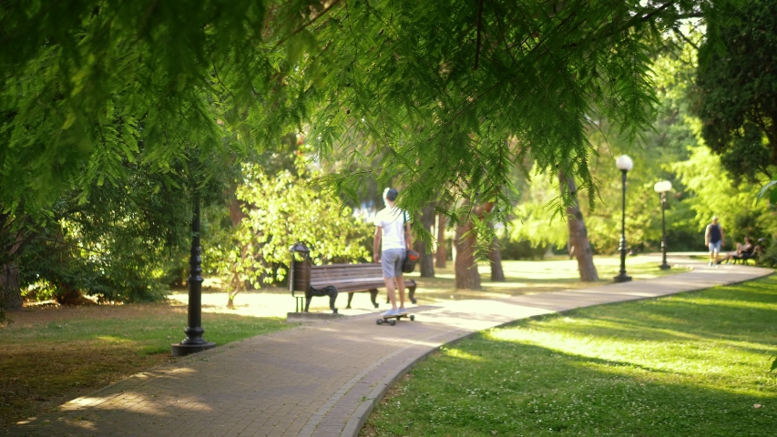 young handsome man in a helmet rides a electric skateboard in a beautiful summer park