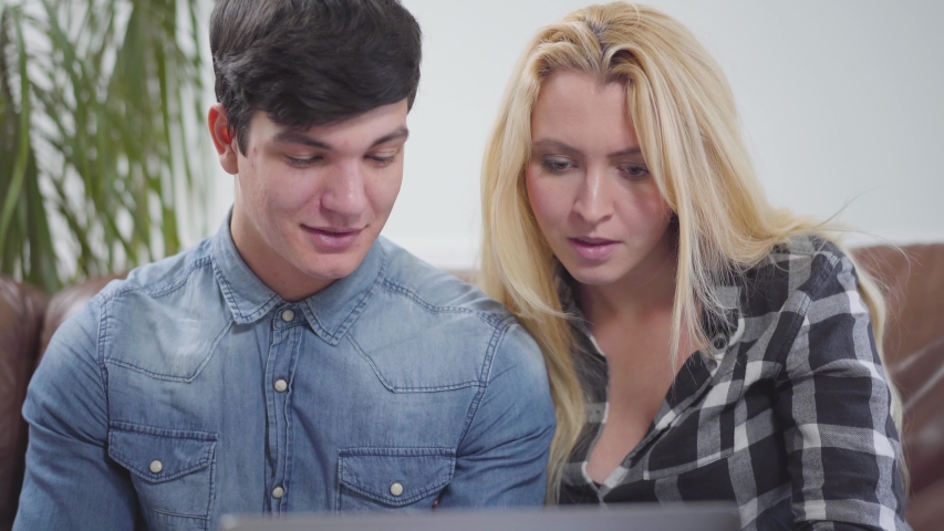Cute couple sitting in front of a laptop at home. Portrait of a brunette man and blond woman discussing the project on the notebook. Working with gadgets