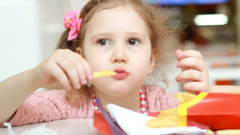 Child girl eating fast food french fries in a cafe. Portrait closeup