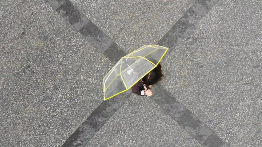 young pretty woman at city square with transparent yellow umbrella smiling overhead view. rainy weather