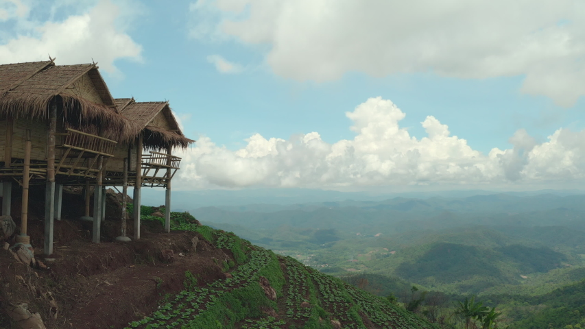 Aerial panoramic shot, homestay accommodation near vegetable bed with cloudy sky at hilltop. Holidays rustic resort. Organic vegetable farm with tourism concept. The overtake shot.