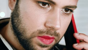 Closeup of adorable homosexual man with bright makeup and red lipstick is talking on his mobile phone