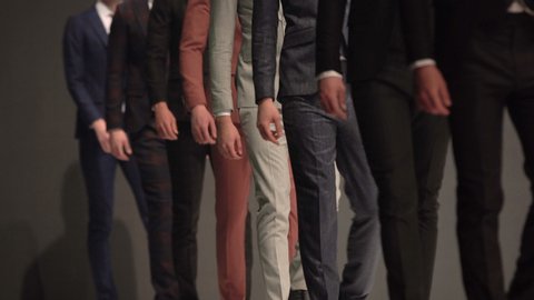 Male models walk the runway in elegant suits during a Fashion Show. Fashion catwalk event showing new collection of clothes. Unrecognizable people.