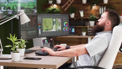 Video editor working in professional software. He uses a dual screen setup and works in modern designed studio office