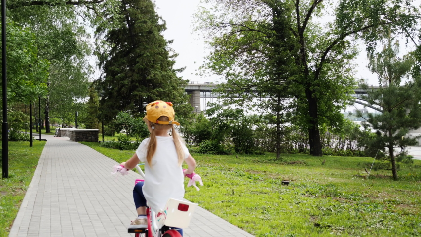 Rear view of little adorable child with pigtails enjoying riding bicycle outdoors