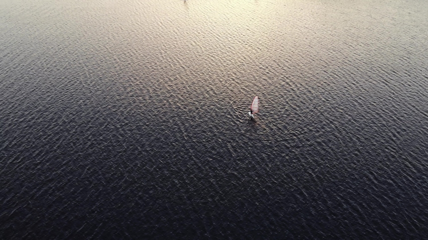 distant windsurfers on sailboards sail on rippling water