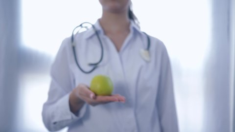 professional expert on food with green apple in hands gives into camera advising healthy diet for wellness, unfocused on white background