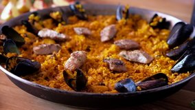 On wooden table is shallow pan hand of chef decorating paella with prawn, slow motion close up video, ripe ingredients of prepared served paella spanish traditional cuisine, food in motion concept