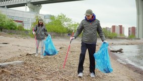 Two young volunteers, man and woman, with trash pickers and bags collecting rubbish on dirty sea coast - Powered by Shutterstock - Get 15% off with code: PIKWIZARD15