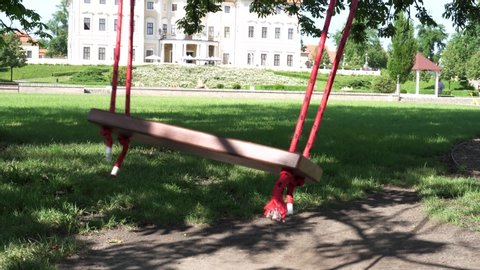 
Empty swing on children playground,Children swing in the park,wooden swing,wooden swing on the lawn. In the background Liblice Chateau Hotel and Conference Center