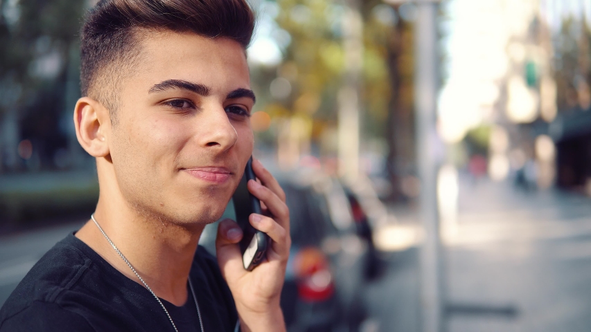 Young fashionable handsome man on the street of modern city talking on a cell phone. Communication concept