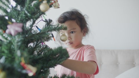 Asian girl are preparing a green Christmas tree for the holiday season in her home. The little girl is decorating the Christmas tree. Stock Video