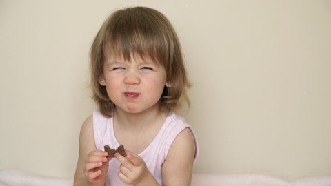 Portrait of little cute blonde child girl bites off with big appetite piece of tasty milky chocolate, eats and smiles