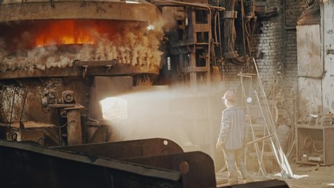 Metal smelting furnace in steel mill. Molten metal Pouring, metallurgy, Steel casting foundry. Steel manufacturing. Hard work in the foundry, worker controlling iron smelting in furnace