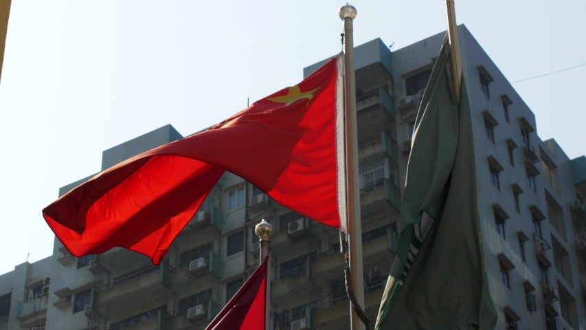 The outside. Against the background of gray buildings, the red flag of China and the green flag of Macau flutter in the wind. It